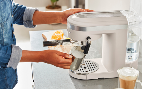 Woman frothing milk with a steam wand on a white espresso machine