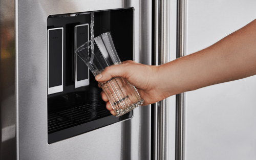 Person filling a glass of water from a refrigerator door