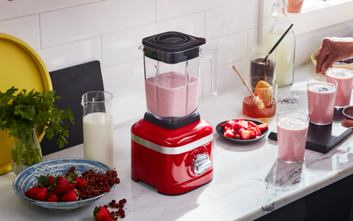 Person preparing strawberry milkshakes with a red blender