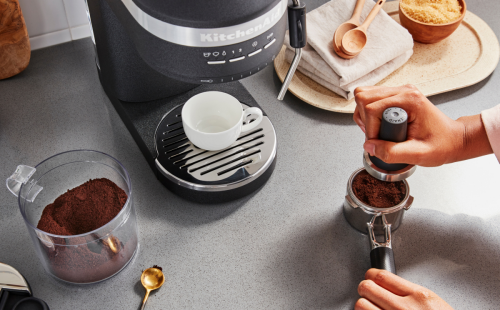 Woman tamping espresso next to machine