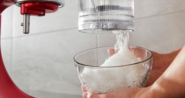 Gros plan sur une personne en train de mettre de la glace pilée dans le bol d'un batteur sur socle KitchenAid rouge.