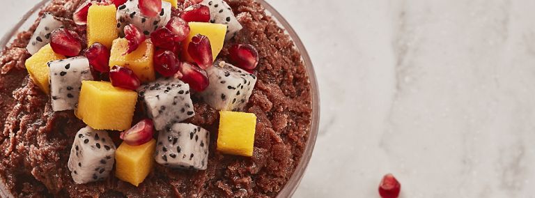 A bowl of bingsu topped with dragon fruit cubes, mango cubes and pomegranates.