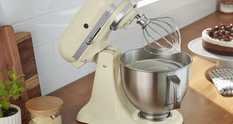 Un batteur sur socle KitchenAid avec la tête inclinée. À côté se trouve un gâteau sur un plateau à gâteau.