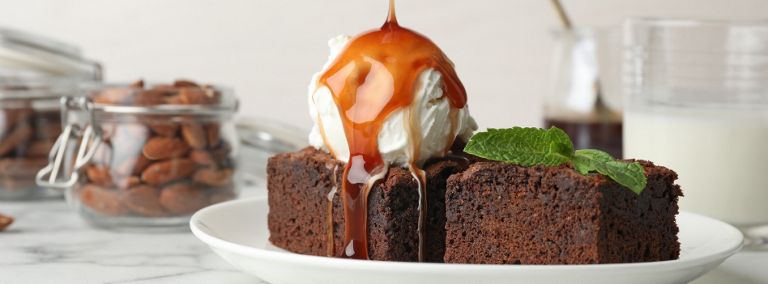 A brownie with a scoop of ice cream on top. Butterscotch is being poured over the ice cream and the brownie. 