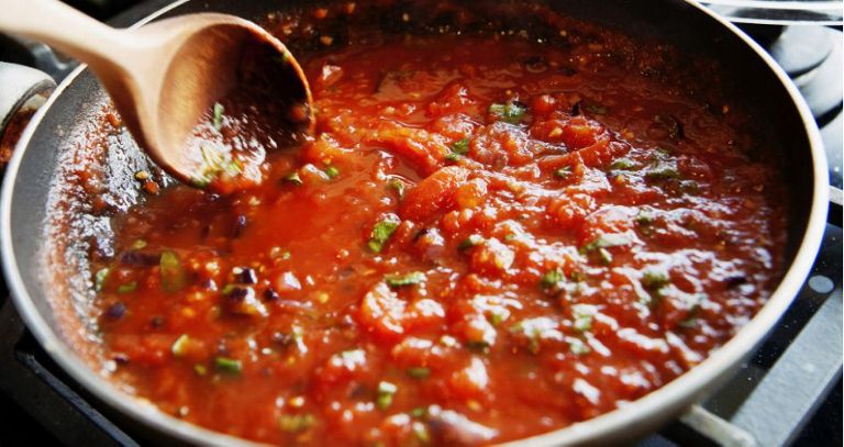 Tomato sauce is stirred while cooking in a pan