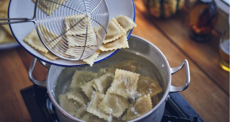 Des raviolis sont retirés d'une casserole d'eau bouillante à l'aide d'une louche.
                      