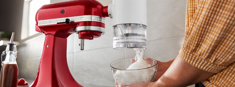  Quelqu'un met de la glace pilée dans le bol d'un batteur sur socle KitchenAid rouge.