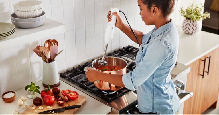 A woman blending soup using an immersion blender