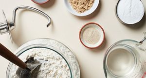  Gently combining ingredients like water, flour, dry yeast, and sugar into a transparent mixing bowl. 